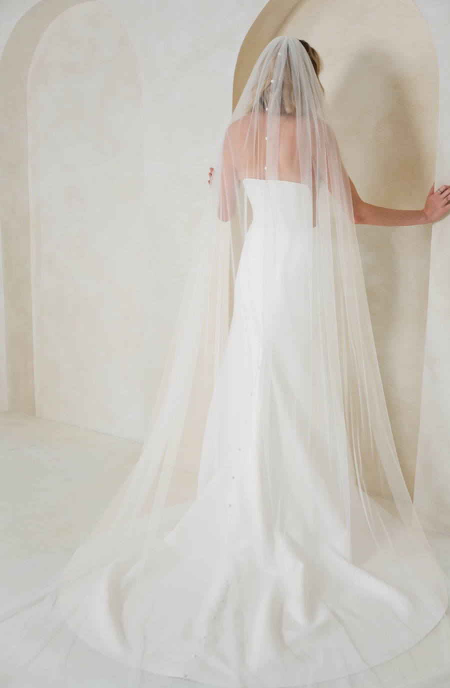 Model is wearing a strapless wedding dress with sheer nude side panels and a high slit