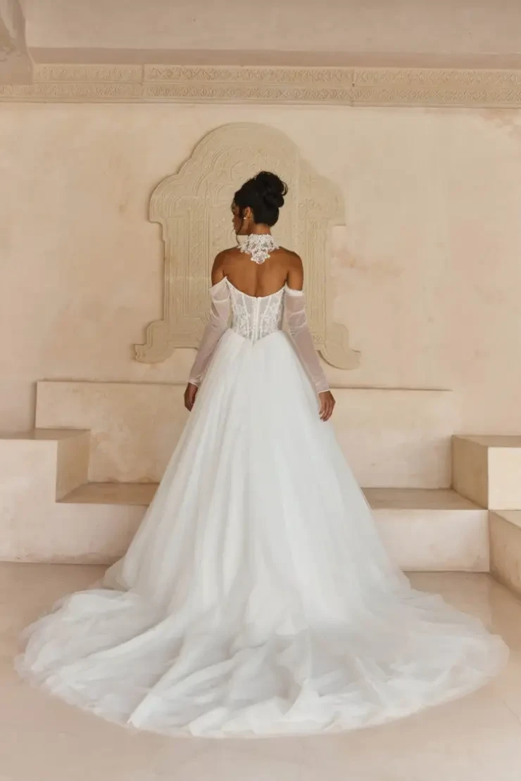 Model is wearing Larkin, a full tulle ball gown with a ruched long-sleeve bodice, beaded Chantilly lace, and optional beaded collar.