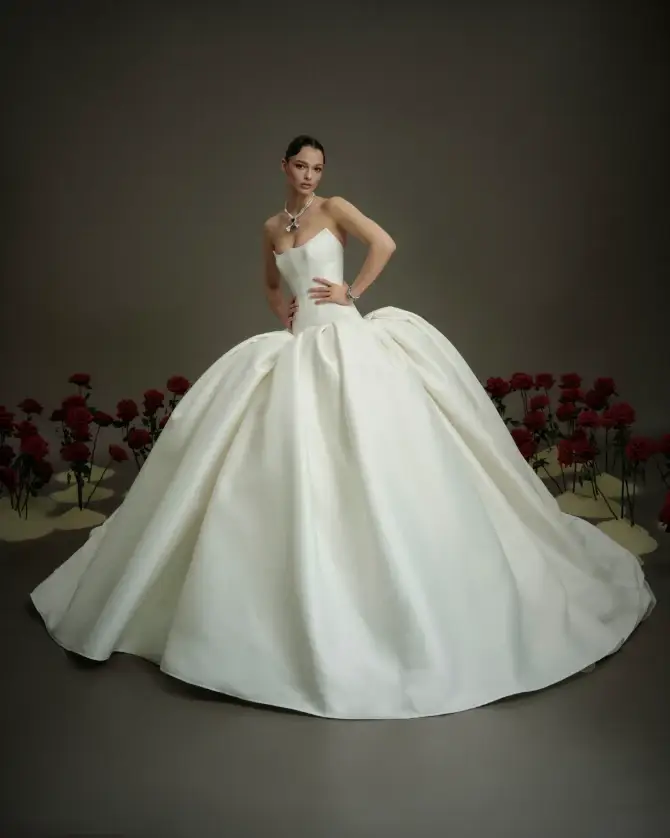 Model is wearing a strapless ball gown with a pointed bodice and voluminous skirt