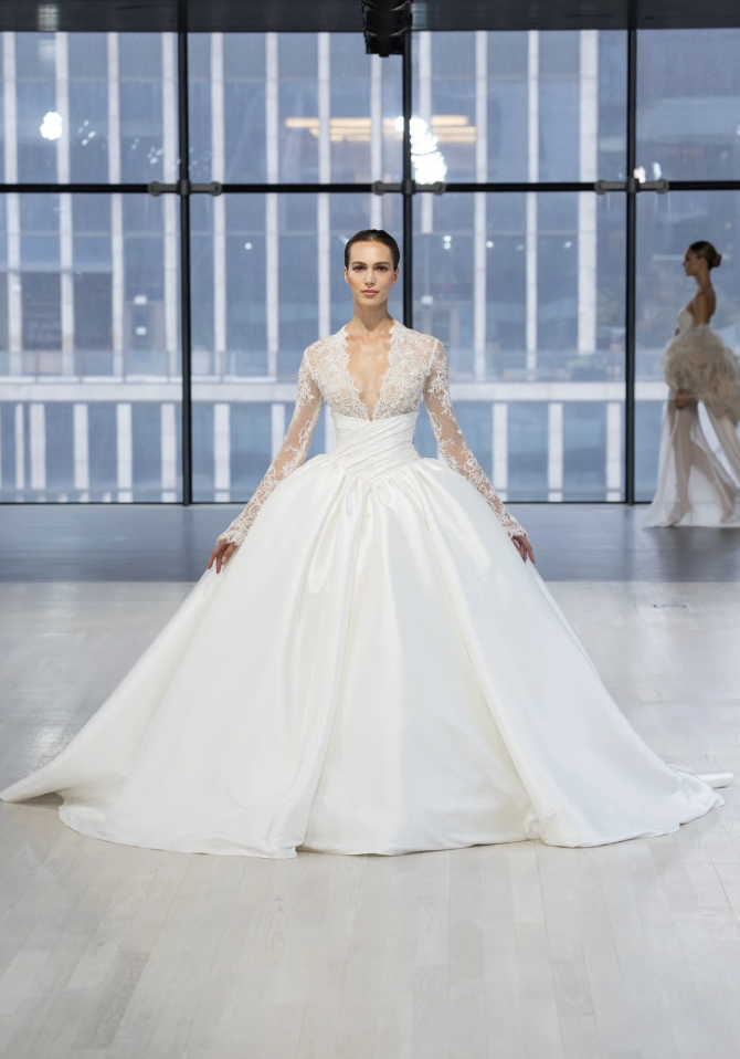 Model is wearing a long sleeve ball gown wedding dress with a plunging neckline