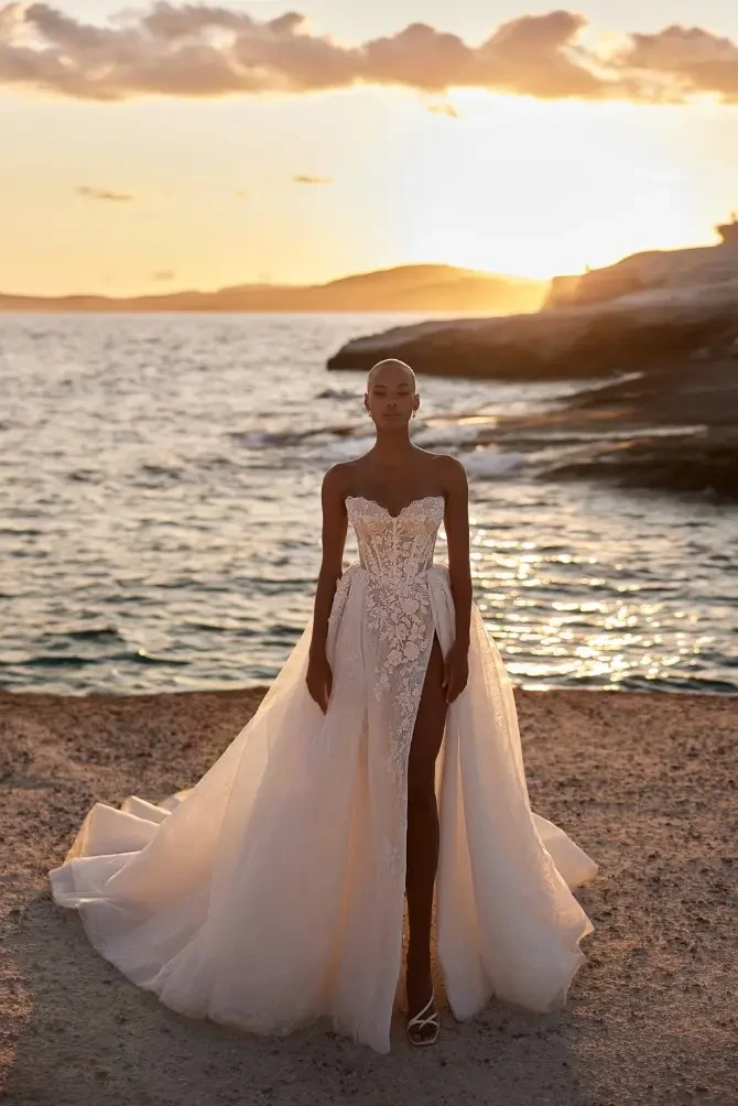 Model is wearing an a-line wedding dress with a voluminous skirt and a strapless sweetheart corset bodice with floral embellishments 