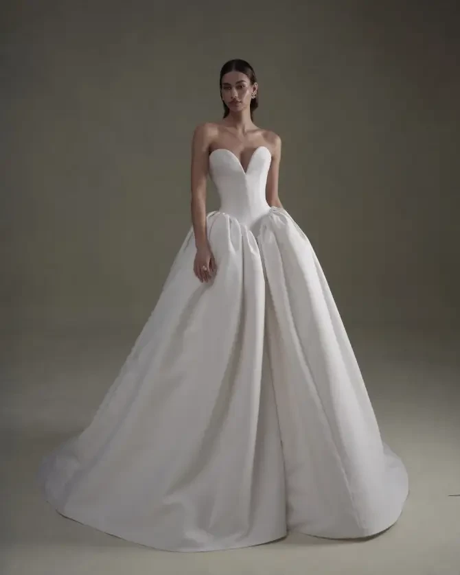Model is wearing a strapless ball gown featuring a sweetheart neckline and contoured basque waist