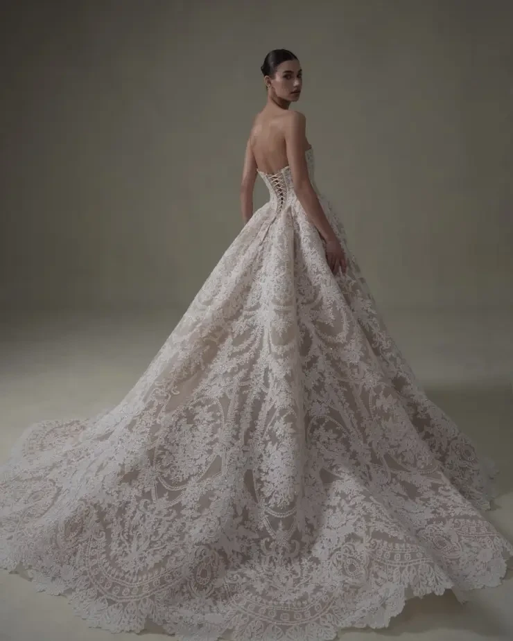 Model is wearing a strapless lace ball gown with a nude underlay and high slit