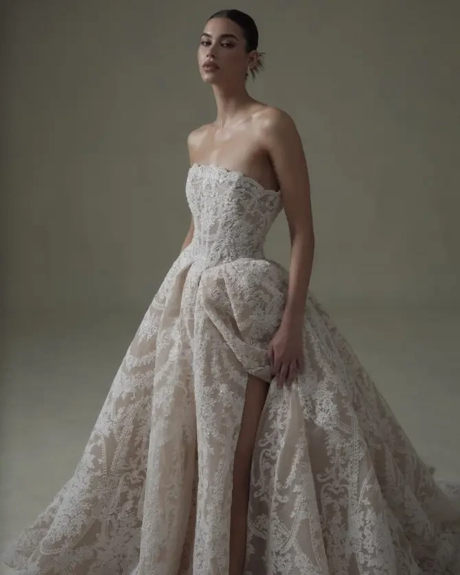 Model is wearing a strapless lace ball gown with a nude underlay and high slit