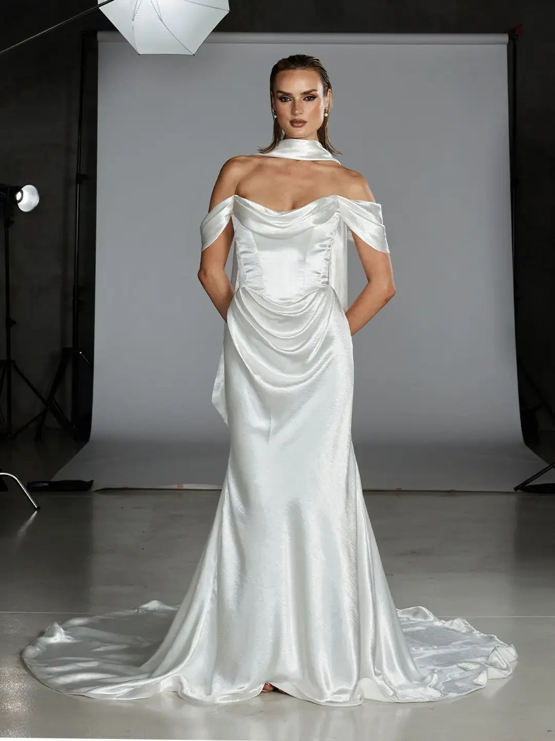 Model is wearing an off the shoulder satin fit and flare wedding dress with a corset bodice