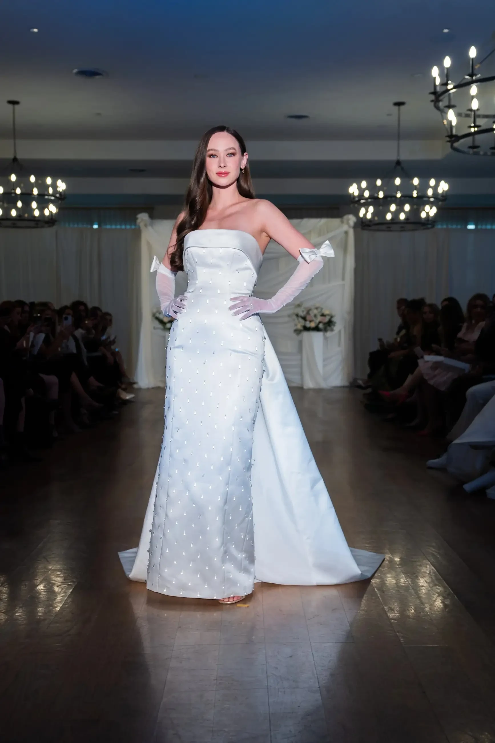 Model is wearing a strapless sheath wedding dress with gloves and a foldover neckline