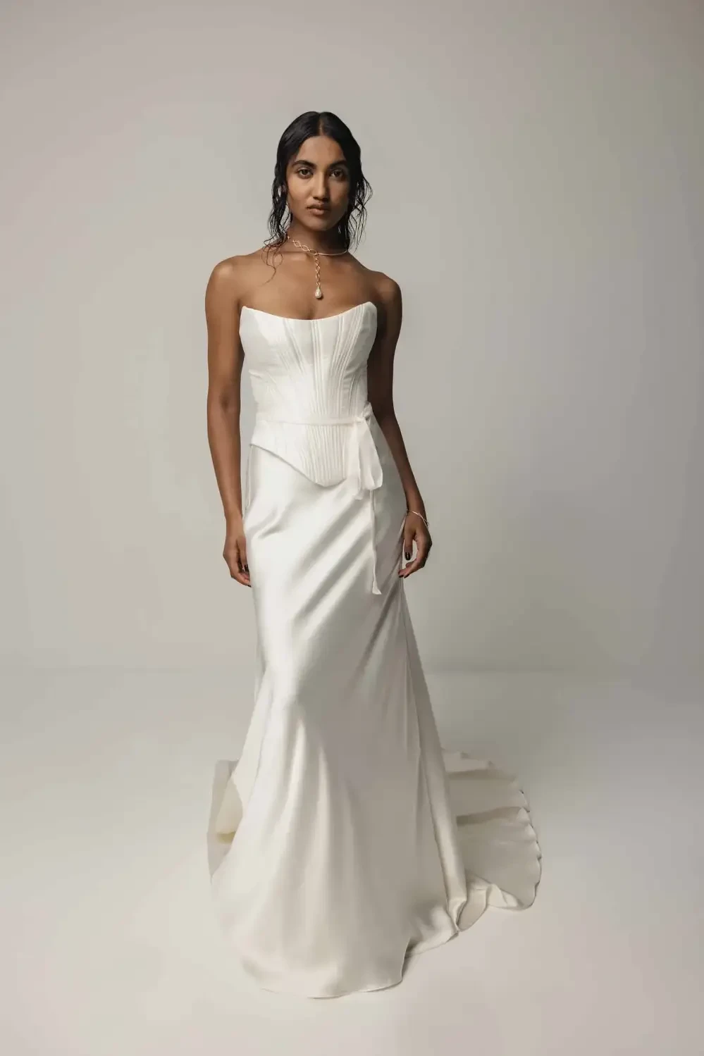 A woman wearing a strapless white gown, standing confidently against a neutral background.